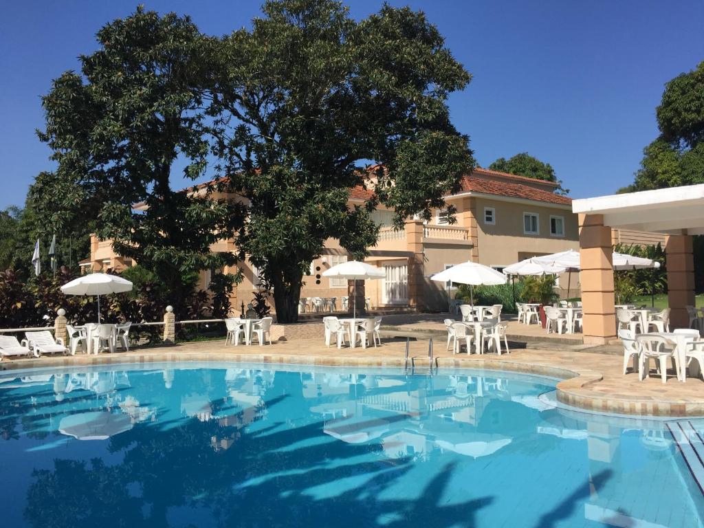 Área externa do Hotel La Ponsa Itatiaia. Na parte da frente está a piscina do hotel, em frente a piscina estão diversas mesas com cadeiras e guarda-sóis e ao fundo é possível ver uma parte do hotel.