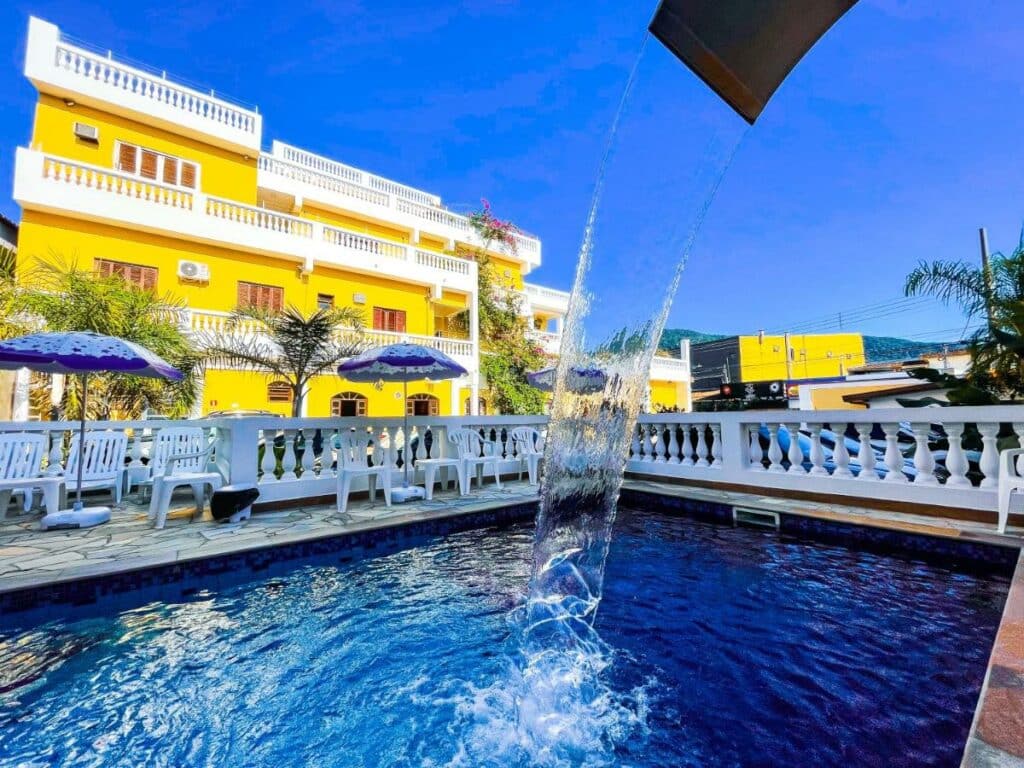 Área externa com piscina do Hotel Parque Atlântico, um dos hotéis em Ubatuba, com cascata de água e cadeiras nos arredores
