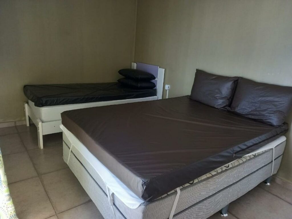 Quarto da Linda Vista e Som das Ondas, um dos airbnb em Caraguatatuba. Uma cama de solteiro está encostada na parede ao lado esquerdo, e uma de casal fica ao seu lado. As duas camas tem travesseiros.