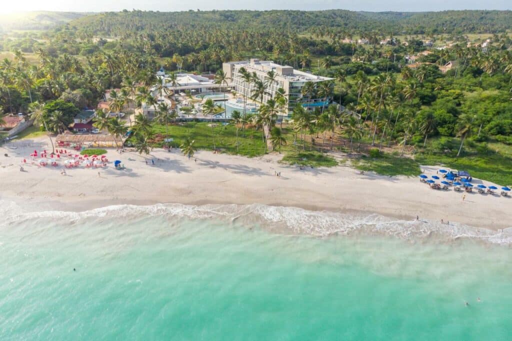 Praia de Antunes com areia extensa branca e o hotel Maragogi Brisa Exclusive cercado por árvores à beira-mar