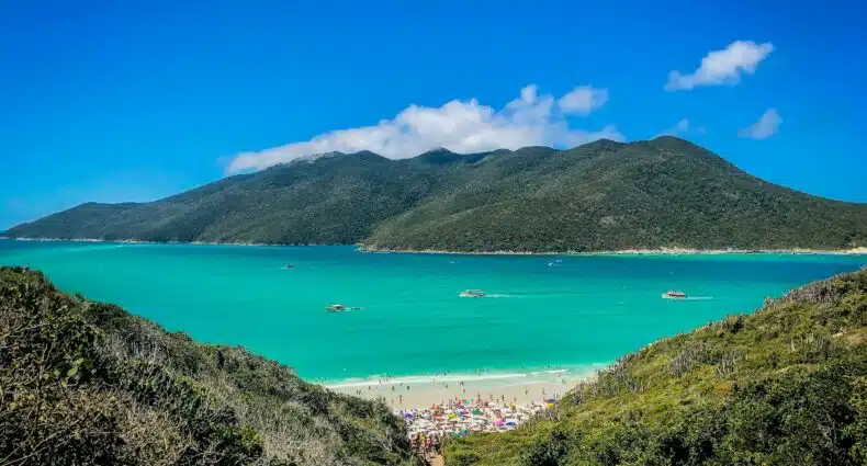 Praia do Atalaia em Arraial da Ajuda, que tem uma entrada muito estreita por entre muita vegetação, o mar é verde e faixa de areia branca, para representar Região dos Lagos