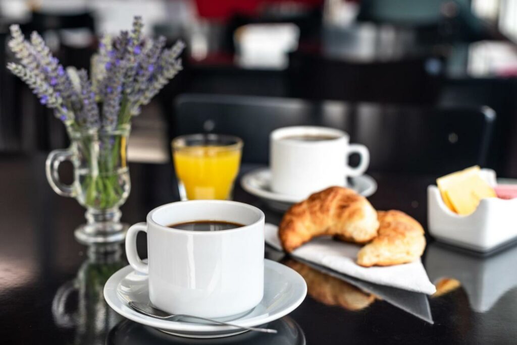 Mesa de café do Pudu Lodge com xicara de café a frente ao fundo dois croissant e mais ao fundo um copo de suco e uma xicara.