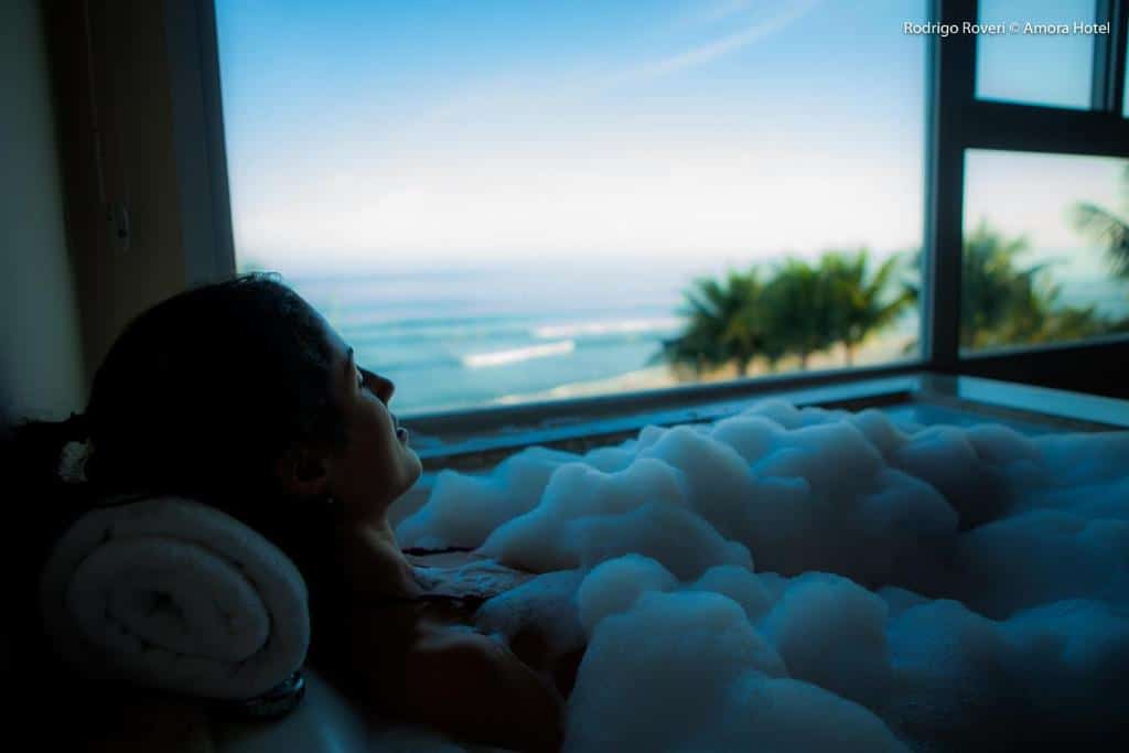 Mulher deitada na banheira no Amora Hotel  no final do dia com vista para o mar.
