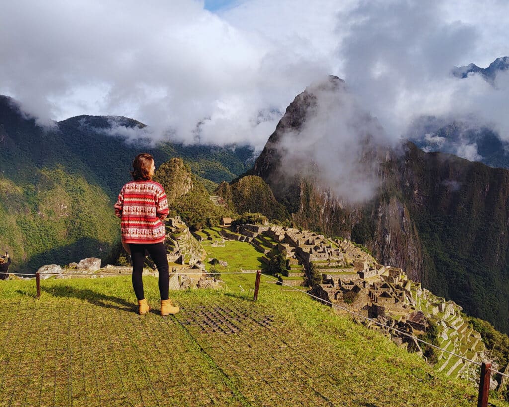 mulher em pé, de costas para a câmera, olhando para o vale abaixo de si de onde é possível enxergar a cidade perdida dos incas: machu picchu.