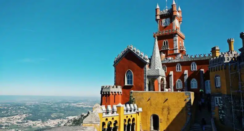 vista de perto do Palácio da Pena, em Sintra, Portugal, em cores fortes amarelas e alaranjadas em pedra com céu azul ao fundo