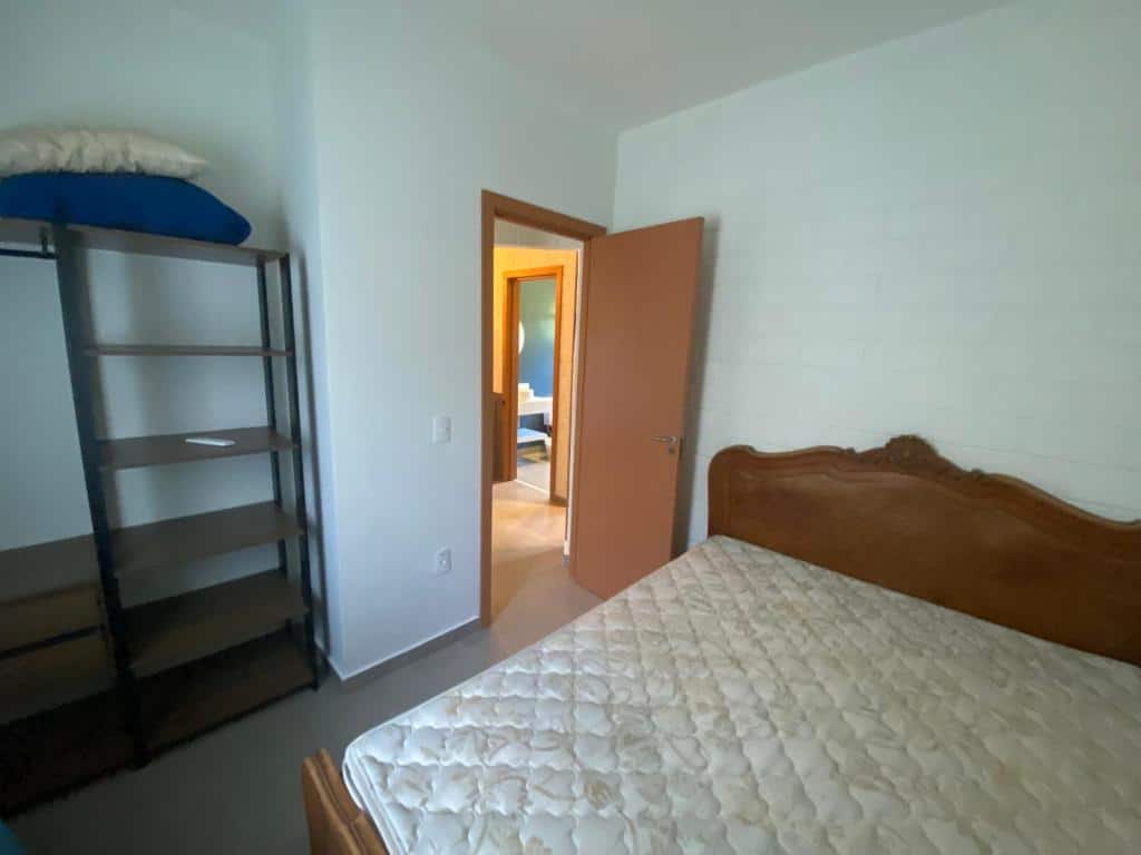 Foto do quarto no Residencial Marina Del Sol. Há uma cama de casal sem lençol na direita, e na esquerda há a porta do quarto e uma estante vazia com prateleiras.
