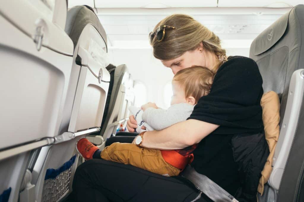 Uma mulher sentada dentro de um aviao com um bebê em seu colo que está segurando uma pequena pelúcia branca