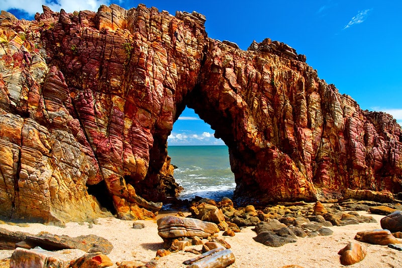 Um dia com o céu bem azul. A foto está mostrando a Pedra Furada, atração turística em uma praia de Jericoacoara.