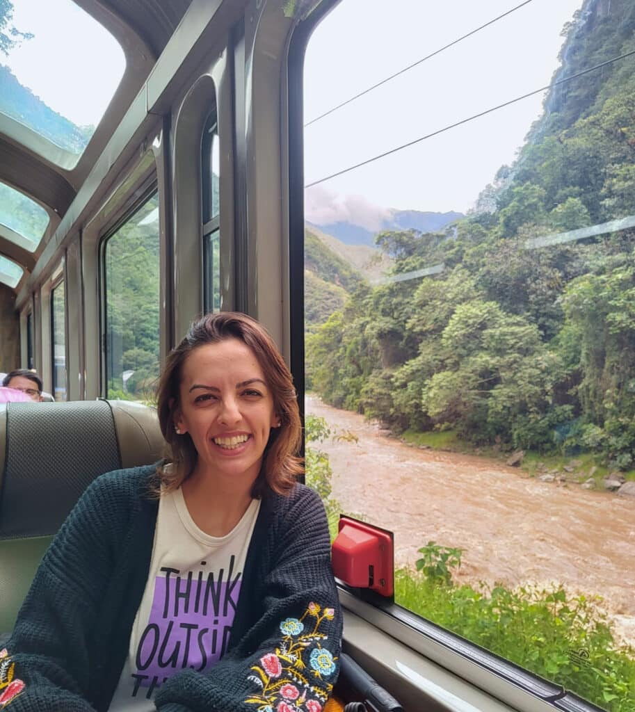 nátalie guimarães sentada ao lado da janela no vagão da peru rail. No lado de fora é possível ver as montanhas peruanas e o rio urubamba
