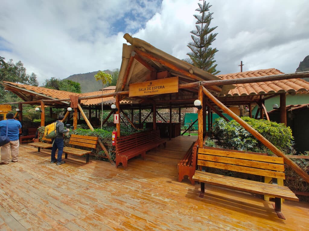 área da sala de espera da Perurail na estação de trem em Ollantaytambo. O espaço é todo rústico, com arquitetura em toras de madeira.