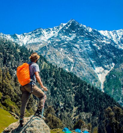 Um homem parado diante de diversas montanhas nevadas, com muita vegetação ao seu redor, para representar por que contratar um seguro viagem