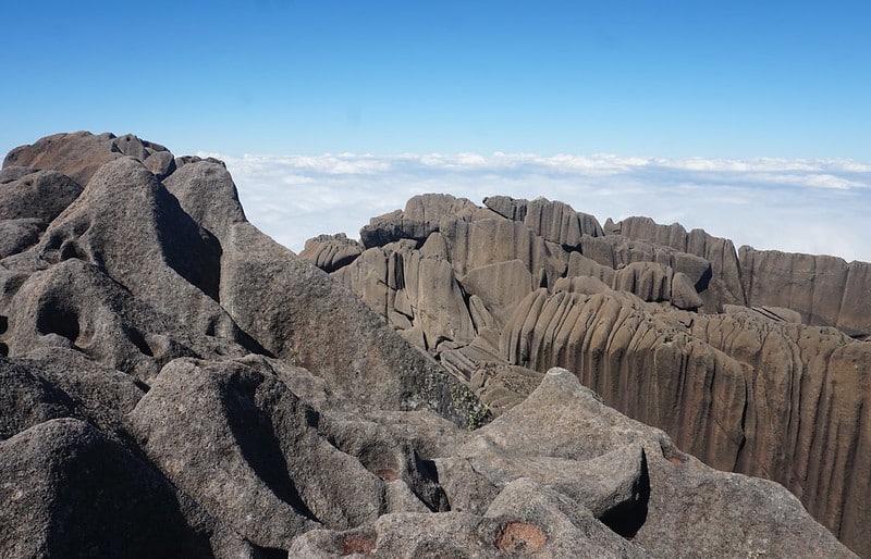 Topo do Pico das Agulhas Negras no Parque Nacional do Itatiaia. Na frente da imagem estão as rochas do topo do pico e ao fundo o céu está azul. Imagem para ilustrar o post airbnb em Itatiaia.