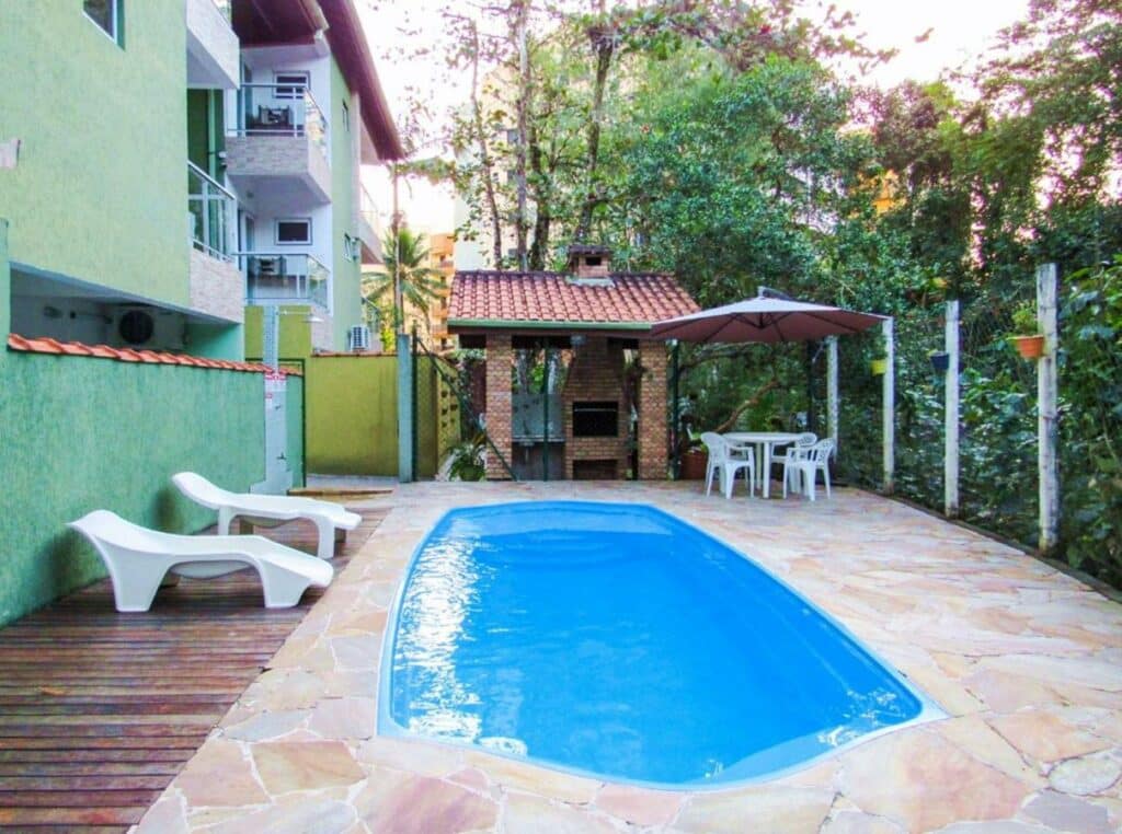 Vista da piscina do Apto c churrasq privativa na Praia de Tabatinga SP durante o dia com piscina a frente e do lado esquerdo duas cadeiras e do lado direito ao fundo uma mesa com quatro cadeiras.