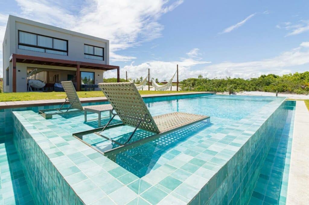 Piscina ao ar livre da SA05 Excelente Casa 5 Suítes – Condomínio Reserva de Sauípe durante o dia com duas cadeiras na borda da piscina e ela a frente.