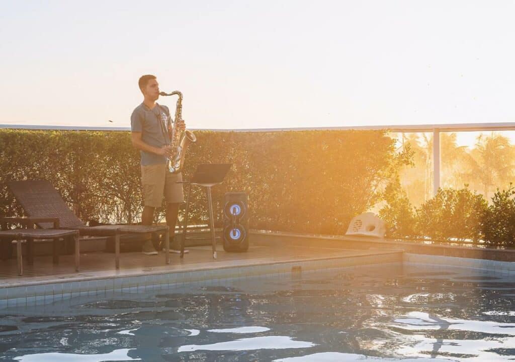 Homem tocando saxofone na beira da piscina do Hotel Ponta Verde Francês, com o raio do pôr do sol refletindo nele