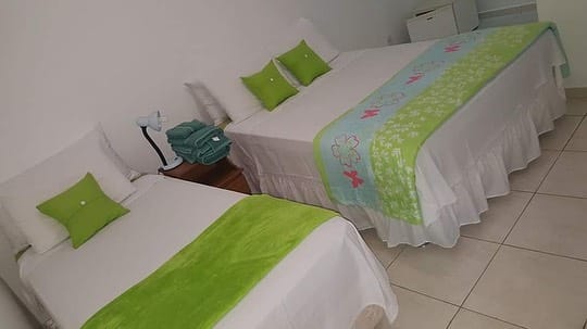 Quarto da Pousada Del Mare di Ponta Negra. Uma cama de casal e uma cama de solteiro, entre elas uma cômoda com um abajur. Foto para ilustrar post sobre pousadas em Maricá.