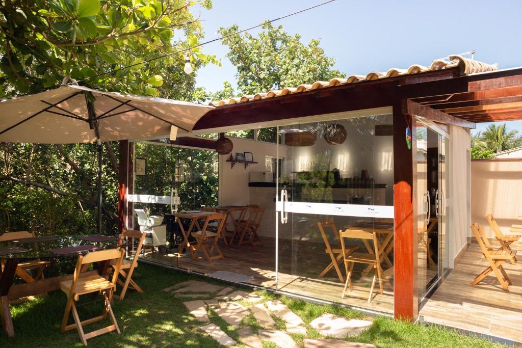 Área externa da Pousada Vila da Praia. Um jardim com mesas, cadeiras e guarda-sóis, atrás mais mesas e o lugar do café da manhã.