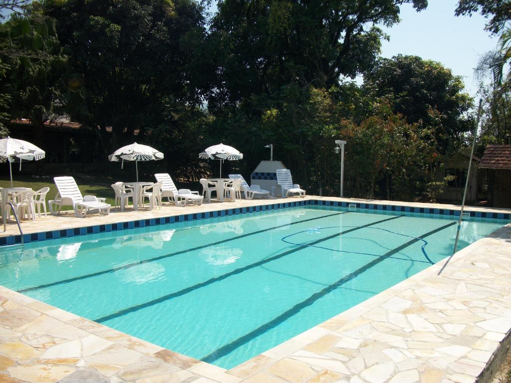 Área externa da Pousada Ypê Amarelo. No lado direito da imagem está a piscina da pousada e no lado esquerdo estão algumas mesas, cadeiras e guarda-sóis. Imagem para ilustrar o post airbnb em Itatiaia.
