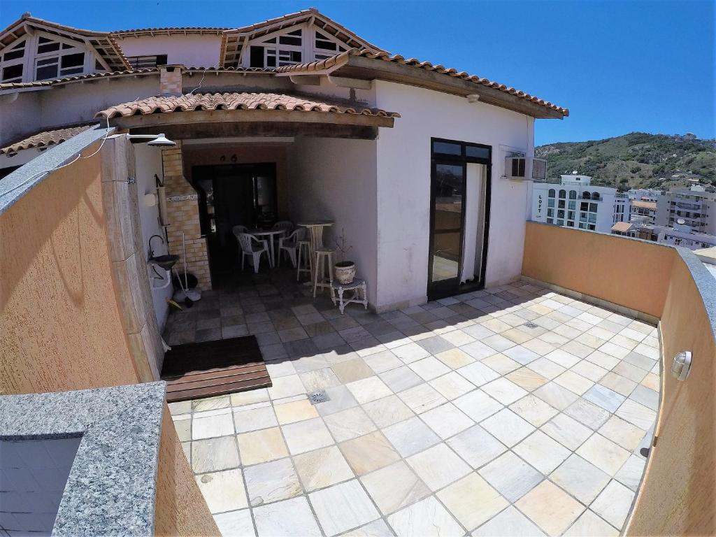 Terraço do airbnb Praia Linda Hospedagem. No canto esquerdo da imagem há em uma área coberta uma churrasqueira, uma pia, uma mesa redonda com quatro cadeiras, uma mesa redonda mais alta com dois bancos e mais a frente há um chuveiro. Já no lado direito há uma porta de correr de vidro que dá acesso ao quarto. Na parte da frente há um espaço vazio e que não é coberto.