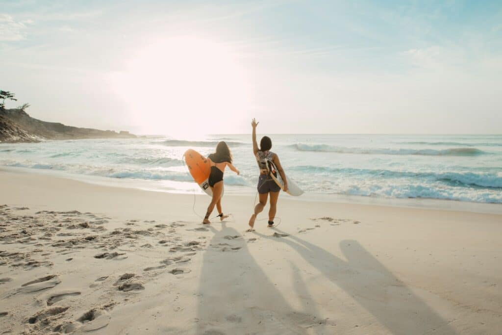 duas mulheres na Prainha, no Brasil, indo surfar no mar para ilustrar o post de Seguro Viagem Sulamerica