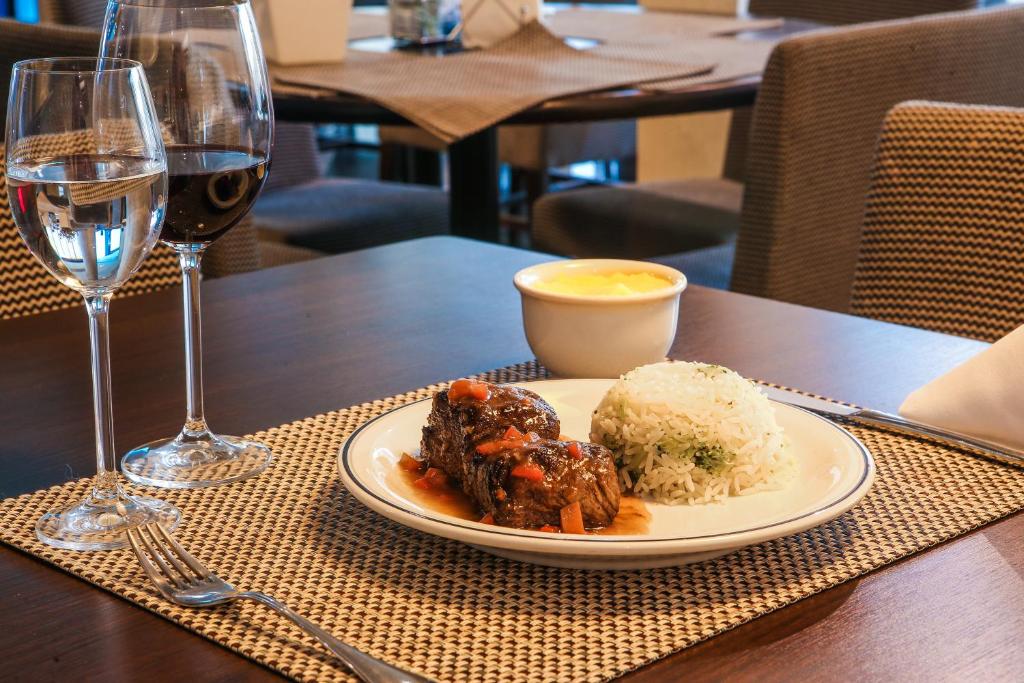 Um prato de comida servido no Hotel Serrano, há arroz com brocólis e uma carne com molho, perto do prato há uma taça com vinho e outra com água, para representar tudo sobre a Paraíba