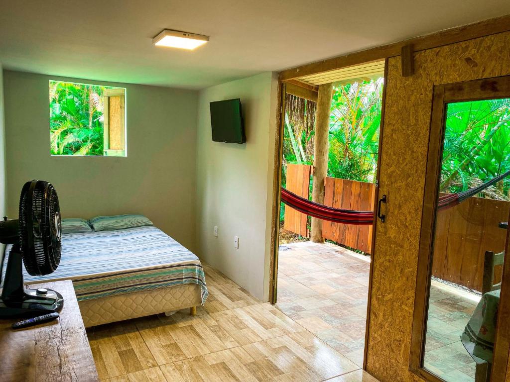 Quarto do AconchegoCaiçara Prumirim com cama de casal do lado esquerdo da imagem no canto ao fundo, do lado esquerdo da cama na parede uma TV presa. Representa airbnb na praia do Félix.