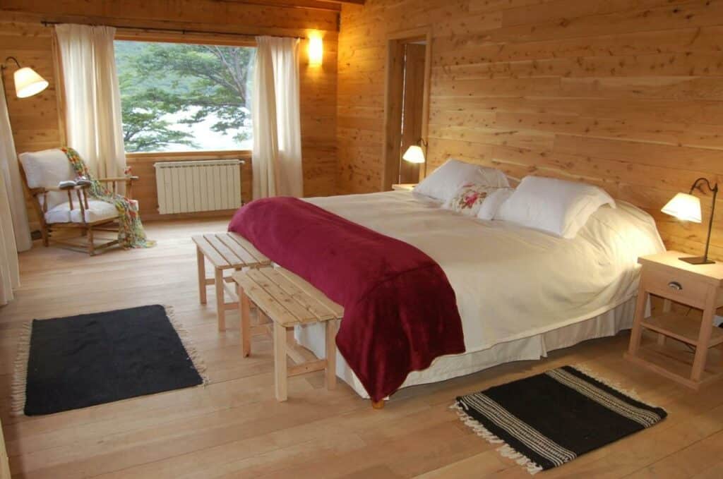 Quarto do Aguas Arriba Lodge com cama de casal do lado direito da imagem com uma cômoda em cada lado com luminária no pé da cama uma cômoda de madeira.