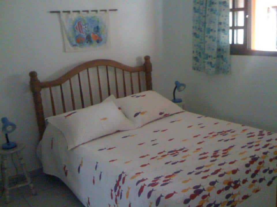 Quarto do Apartamento Sonho Meu com cama de casal do lado esquerdo da imagem, um banco em cada lado da cama com luminária. Representa airbnb na praia da Lagoinha.