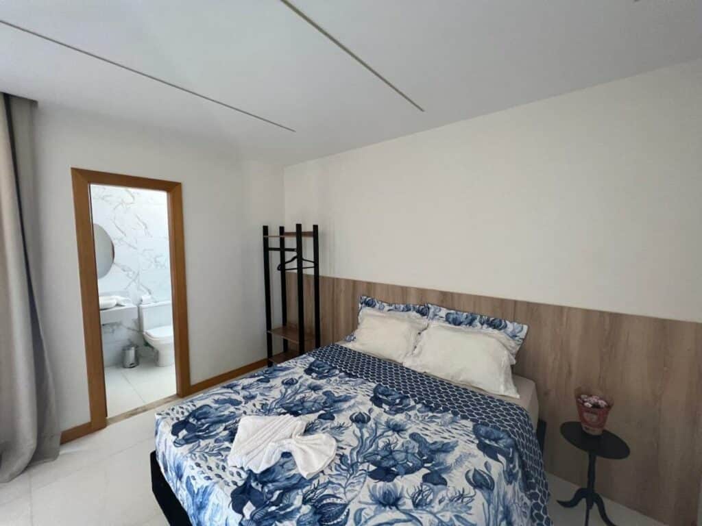 Quarto da Casa da Laguna – Costa do Sauipe com cama de casal a frente no meio e do lado esquerdo da cama uma mesinha com flores. Representa airbnb na Costa do Sauípe