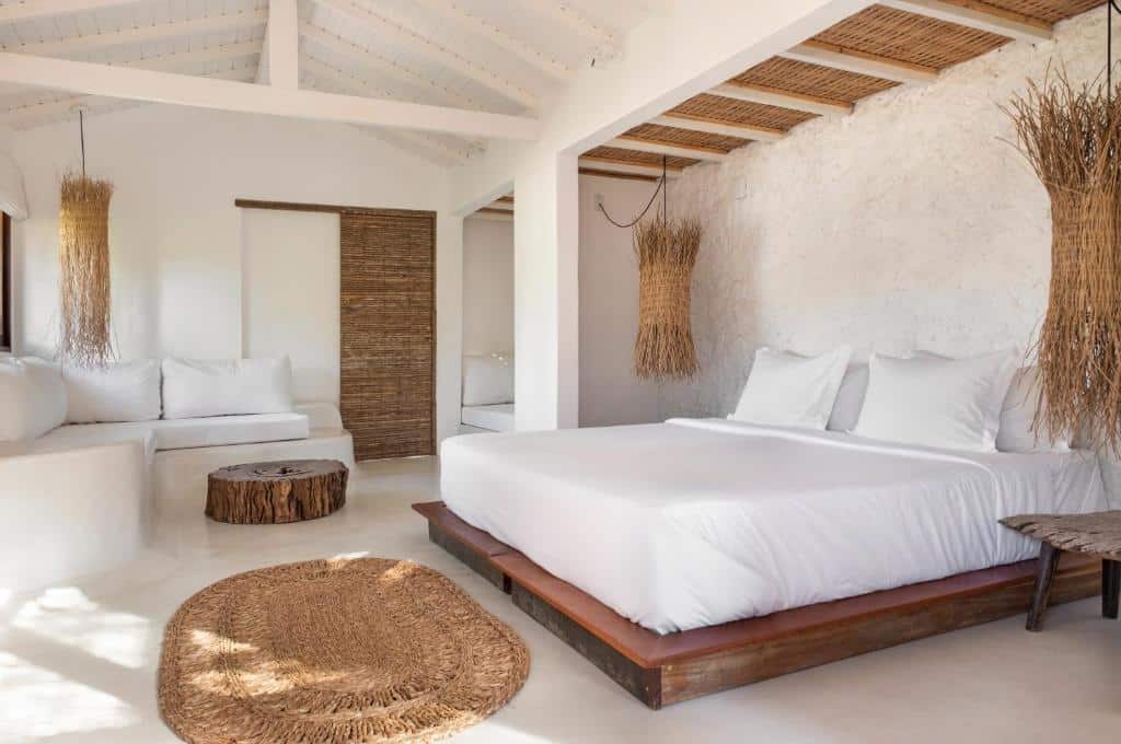 Quarto da Casa das Conchas Caraiva com cama de casal do lado direito da imagem no centro do quarto do lado direito da cama a frente um sofá branco.