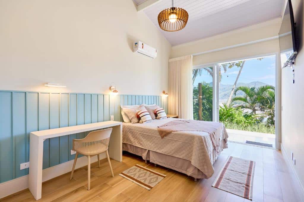 Quarto da Casa de alto padrão com ampla vista para o mar com cama de casal do lado esquerdo da imagem no centro do ambiente com uma cômoda do lado esquerdo da cama e do lado direito uma mesa com cadeira. Representa airbnb na praia do Tenório.