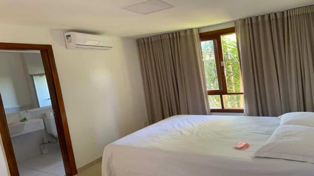 Quarto da Casa de praia na Costa do Sauípe com cama de casal do lado direito da imagem e do lado esquerdo da cama janela com cortinas. Representa airbnb na Costa do Sauípe