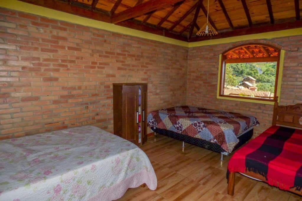 Quarto da Casa do Eduardo ibitipoca mg com três camas de casal, um pequeno guarda-roupa de madeira, paredes de tijolos e uma janela aberta.