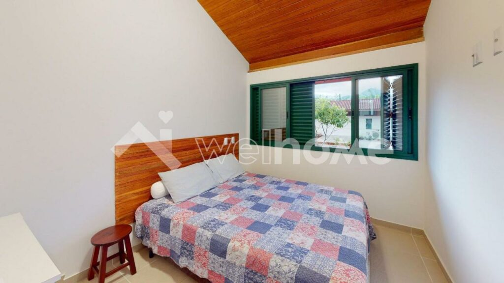 Quarto da Casa em Condomínio na Praia em São Sebastião com cama de casal do lado esquerdo da imagem com um banco do lado direito da cama. Representa airbnb na praia da Juréia.