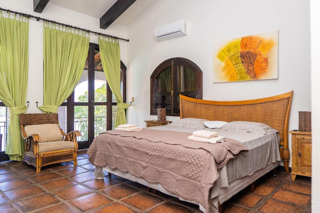 Quarto da Casa luxo, com 9 quartos vista mar Ubatuba com cama de casal do lado direito da imagem no centro do quarto com uma cômoda em cada lado com luminária e do lado direito da imagem uma poltrona. Representa airbnb na praia do Tenório.