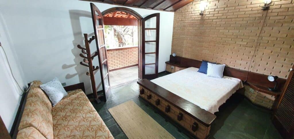 Quarto da Casa na Praia Lagoinha – 300 metros da praia com sofá do lado esquerdo da imagem e em frente uma cama de casal. Representa airbnb na praia da Lagoinha.