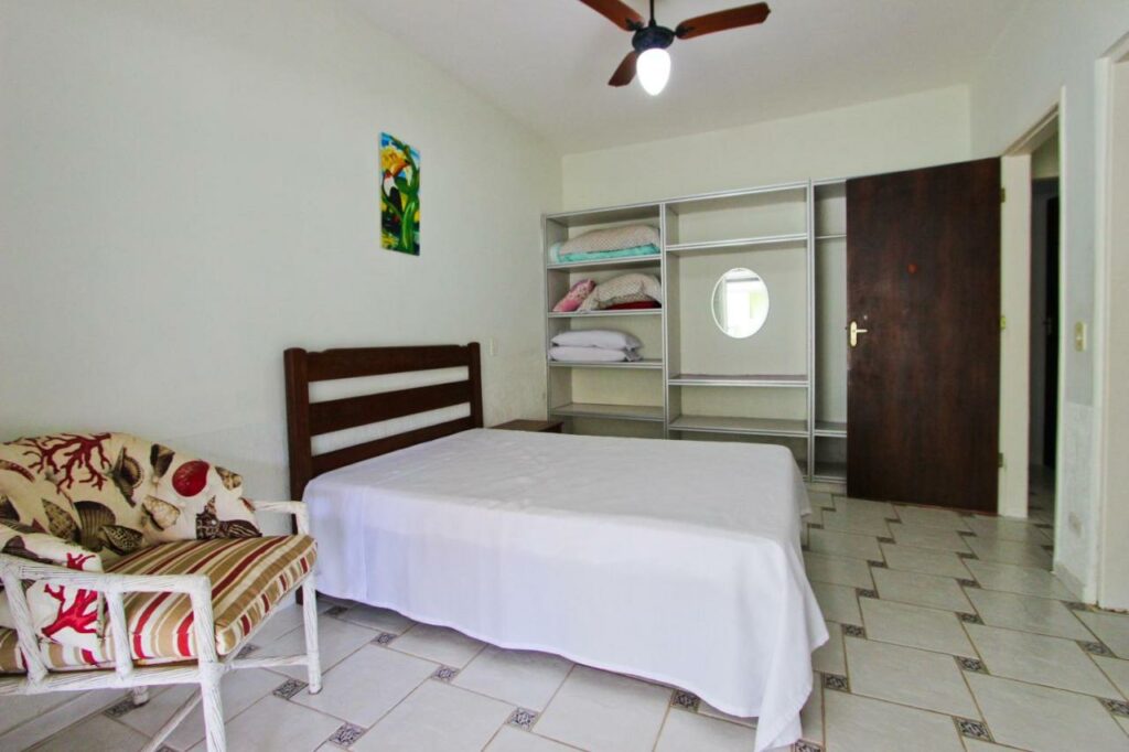Quarto da Casa temporada Tuco e Tuca com cama de casal do lado esquerdo da imagem com uma poltrona do lado direito da cama e do lado esquerdo uma cômoda. Representa airbnb na praia da Lagoinha.