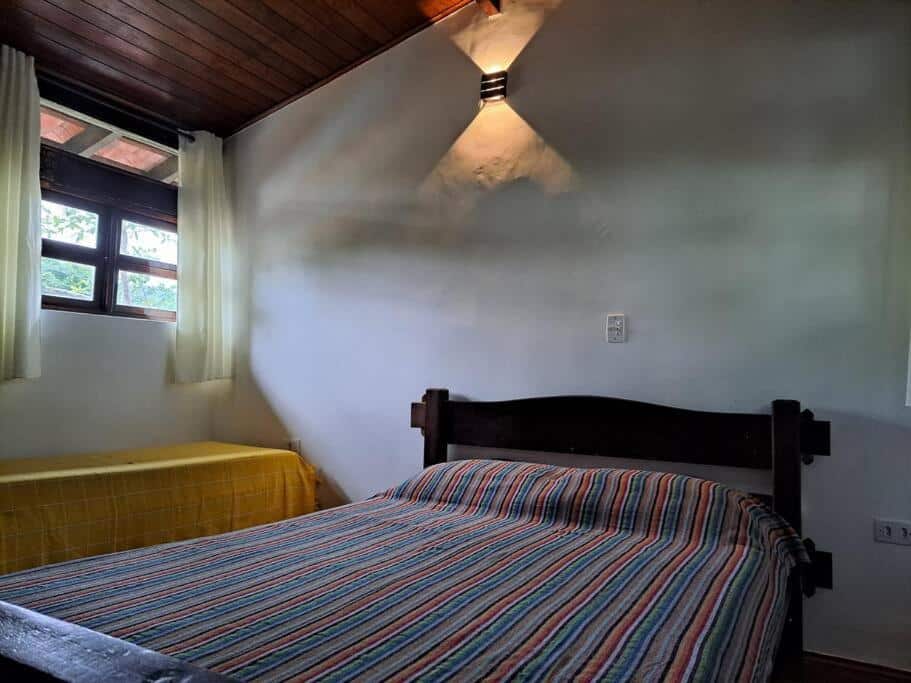 Quarto do Chalé rústico a poucos metros da praia de Lagoinha com cama de casal do lado esquerdo da imagem e do lado esquerdo da cama uma cama de casal. Representa airbnb na praia da Lagoinha.
