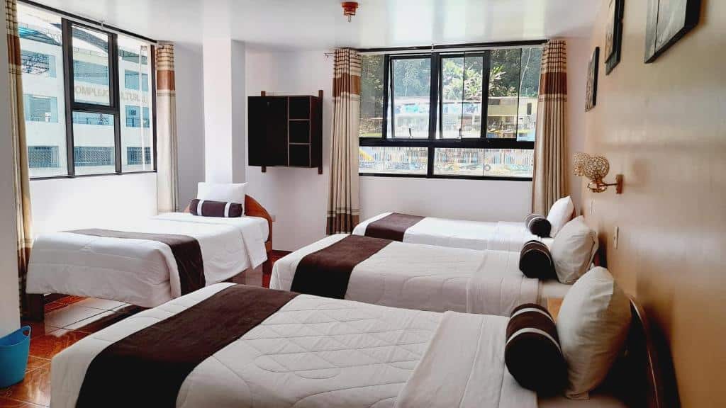 quarto do EL Tambo com quatro camas de solteiro e duas janelas amplas que dão vista para o centro da cidade de Machupicchu.