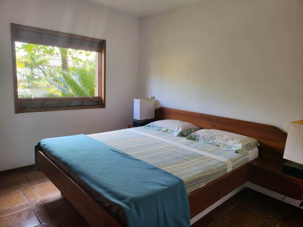 Quarto do Green Toque-Toque com cama de casal no centro e em cada lado da cama uma cômoda com luminária. Representa airbnb na praia de Santiago. 