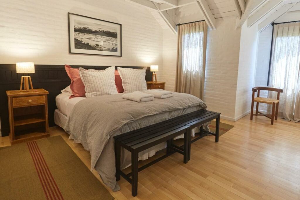 Quarto do Hosteria El Puma com cama de casal do lado esquerdo da imagem com duas cômodas ao lado da cama com luminária. Representa hotéis em El Chalten.