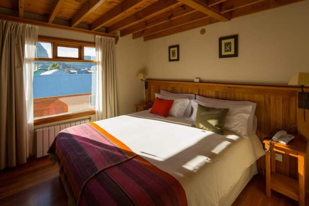 Quarto do Hosteria Senderos com cama de casal do lado direito da imagem com uma cômoda em cada lado da cama. Representa hotéis em El Chalten.