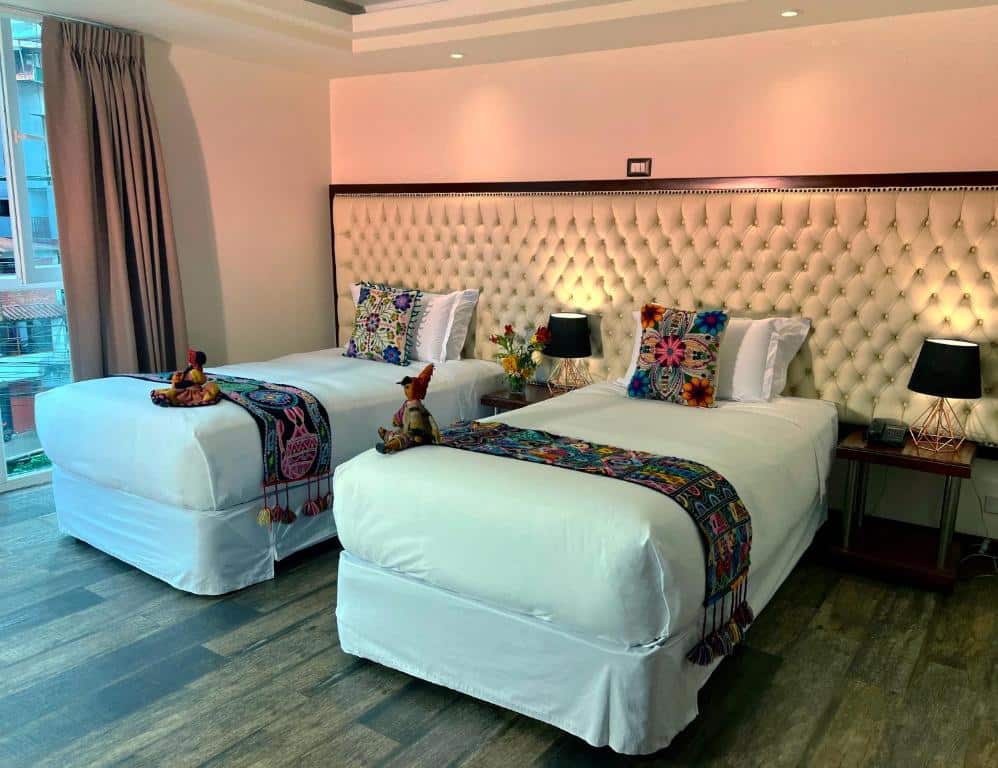 quarto com duas camas de solteiro no jaya machu picchu boutique hotel, com duas cômodas equipadas com abajur em cada lado das camas e lençóis artesanais dispostos em cima das camas.
