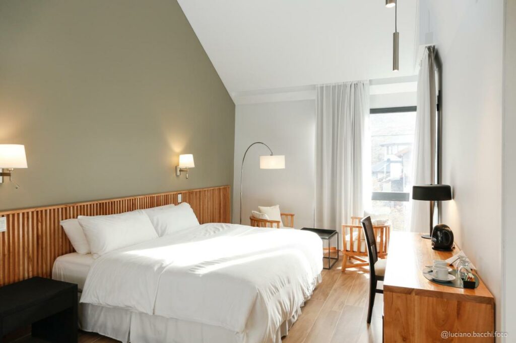 Quarto do Kaulem Hotel Boutique com cama de casal do lado esquerdo da imagem em frente a cama uma cômoda com cadeira.