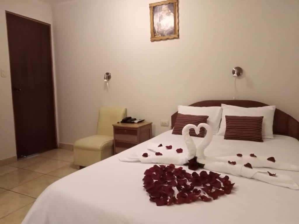 quarto do Machupicchu Dream com cama de casal no canto direito da imagem com duas toalhas dobradas em formato de cisnes, com várias pétalas de rosas vermelhas espalhadas pela cama, formando um coração.