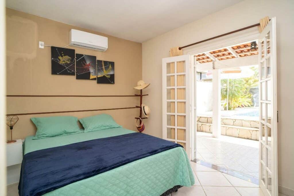 Quarto da Maravilhosa casa no Cond. fechado Morada da Praia com cama de casal do lado esquerdo da imagem no centro do ambiente com uma cômoda com luminária do lado direito da cama. Representa airbnb na praia da Juréia.