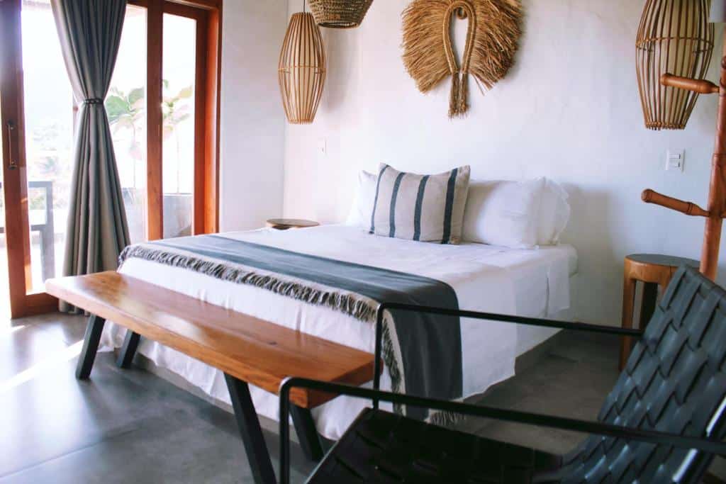 Quarto do Nai com cama de casal no centro do quarto com um banco de madeira em cada lado da cama, no pé da cama um banco comprido de madeira. Representa airbnb na praia de Santiago.