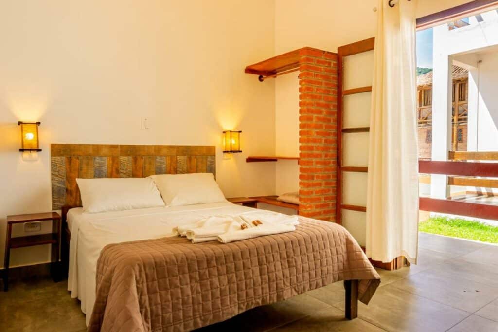 Quarto da Pousada Casarão com cama de casal no centro do quarto com uma cômoda de madeira em cada lado da cama. Representa airbnb na praia de Santiago.