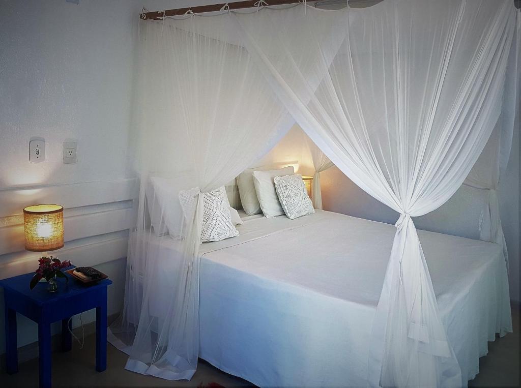 Quarto da Pousada San Antonio Praia com cama de casal do lado esquerdo da imagem no centro do quarto com uma cômoda em cada lado da cama com luminária. Representa airbnb em Caraíva.