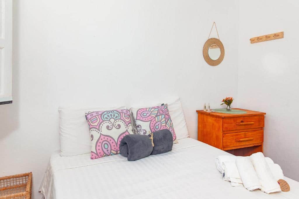 Quarto da Pousada Vila Rosa – Caraiva com cama de casal no centro da foto e do lado esquerdo da cama uma cômoda de madeira. Representa airbnb em Caraíva.